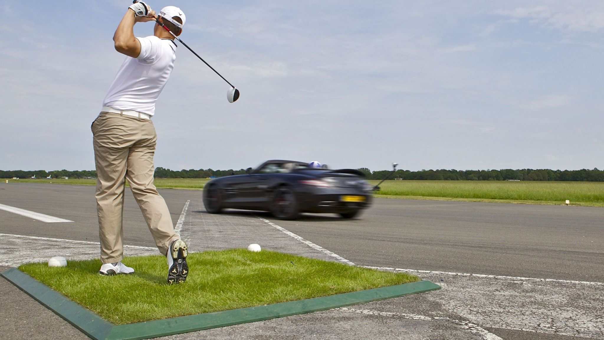 Man playing golf by the side of a race track