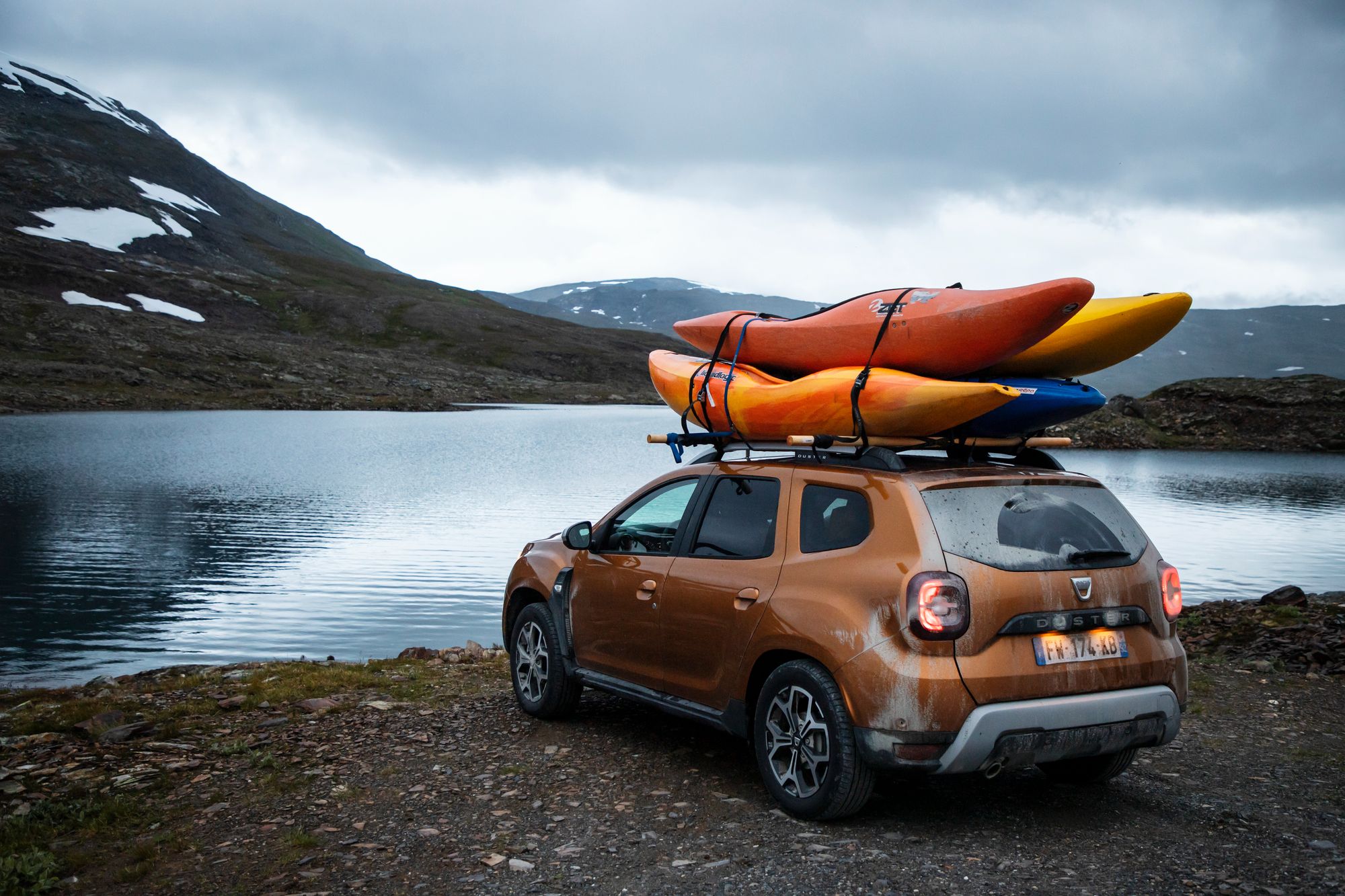 Orange Duster parked by a lake with canoes on the roof