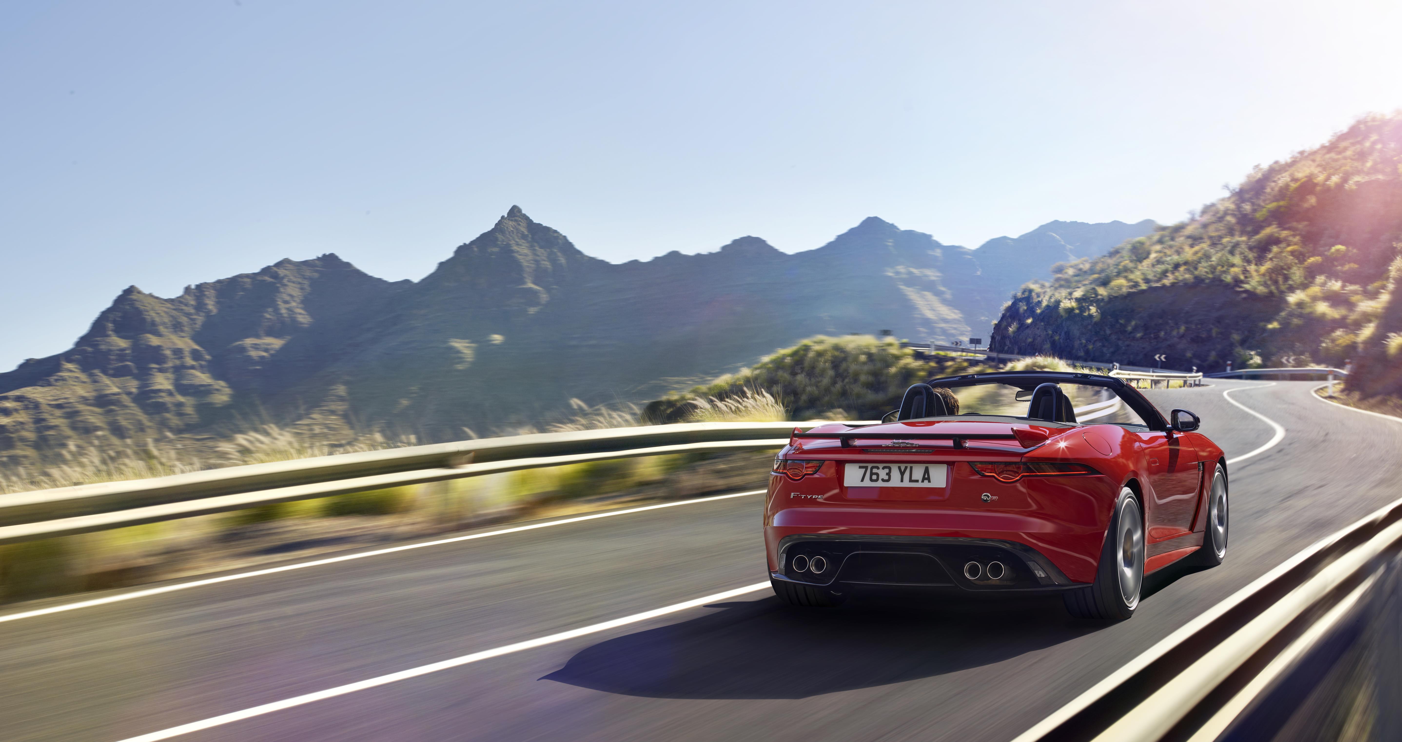Red Jaguar F-Type convertible driving away from you in spectacular countryside