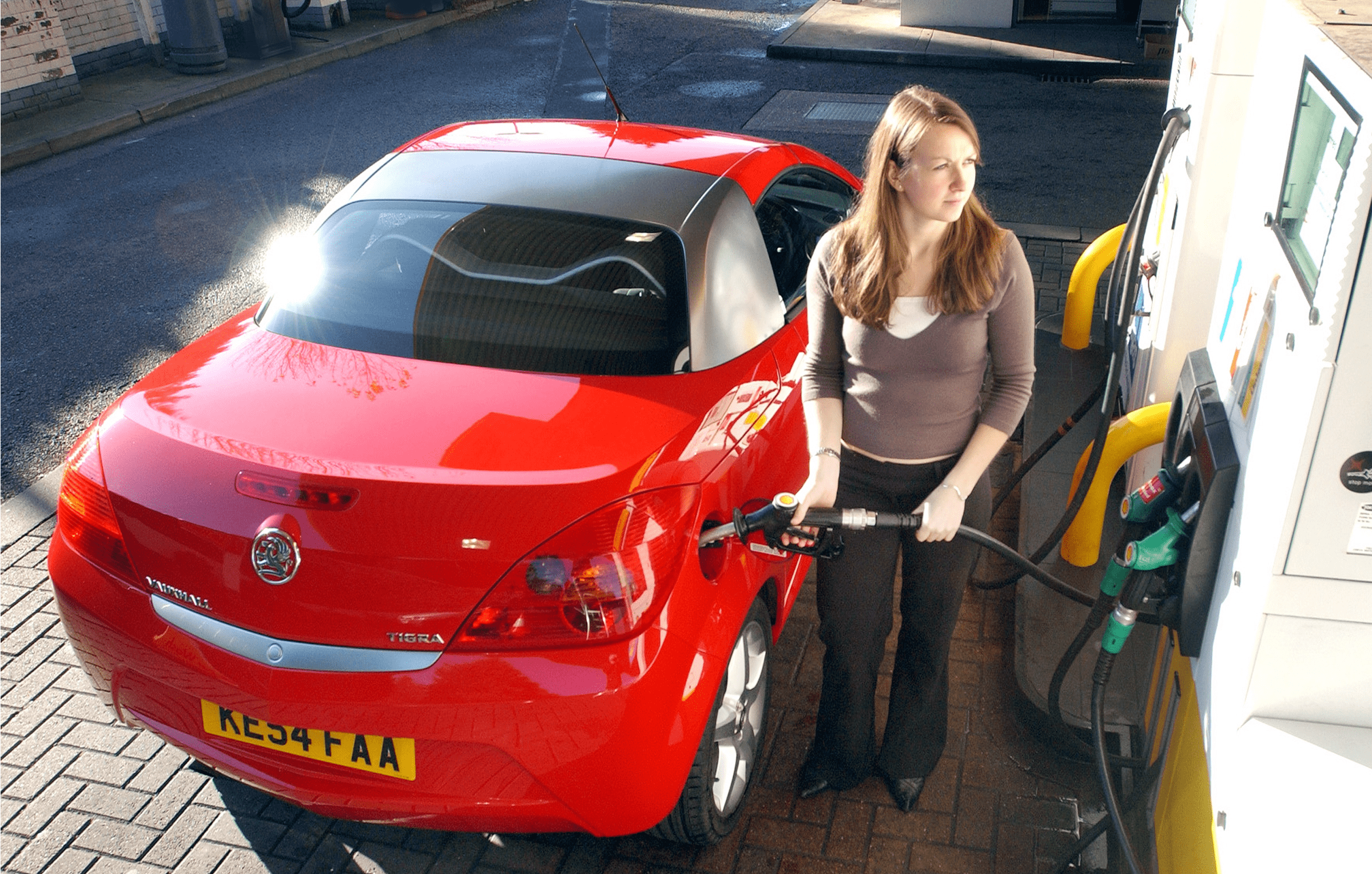Woman filling up a red car with fuel at a a filling station