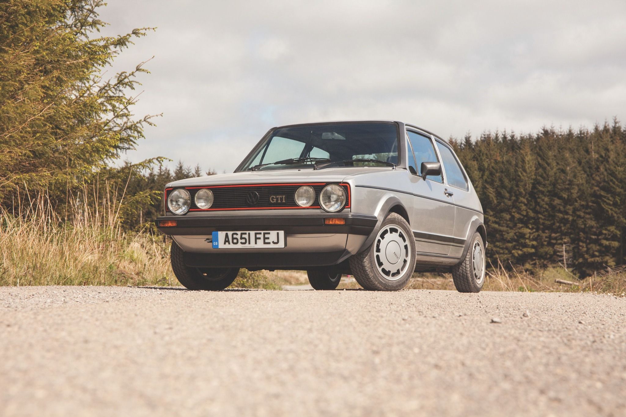 A front view of a MK1 Volkswagen Golf GTI parked on a gravel road