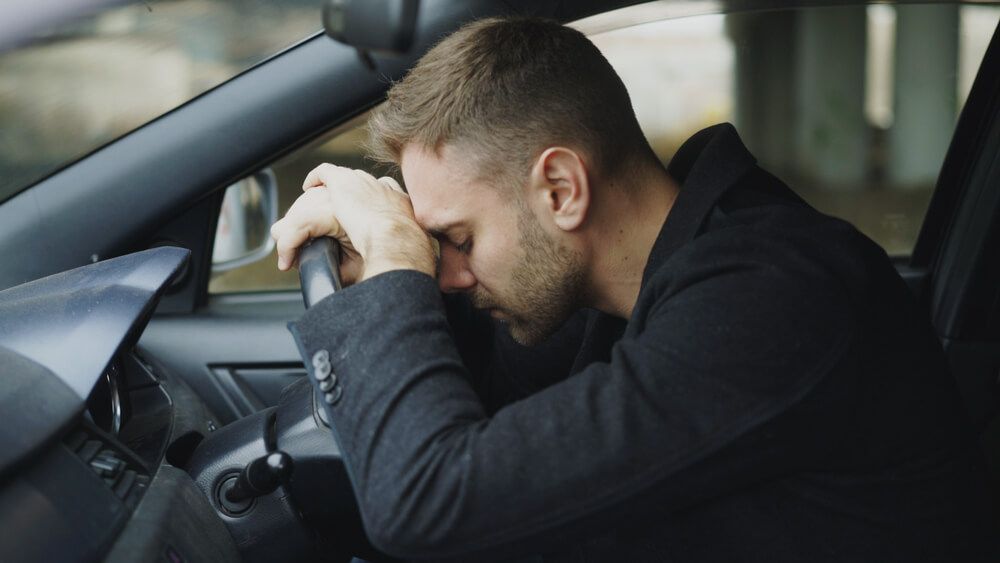man looking stressed with head against steering wheel